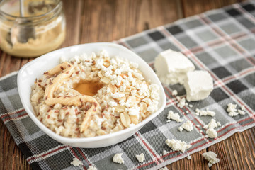 Homemade oatmeal with honey, peanut butter, peanut, flax seeds and cottage cheese on wooden background. Healthy breakfast.