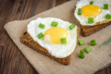 Toast with fried eggs and spring green onion on dark wooden background. Healthy breakfast, lunch, snack or dinner.