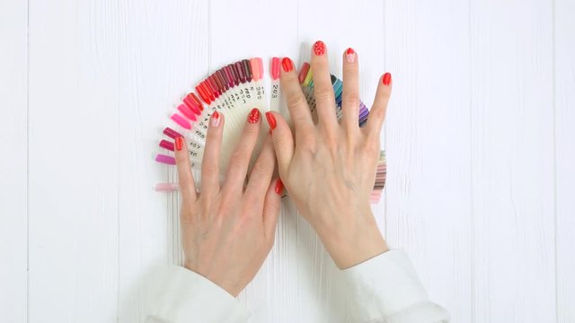 Woman choose red nail color, top view. Female manicured hands choosing nail color on palette, nail samples on table in beauty salon.