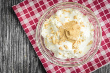 Cottage cheese with sour cream, peanuts and peanut butter on grey wooden background.