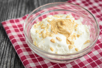Cottage cheese with sour cream, peanuts and peanut butter on grey wooden background.