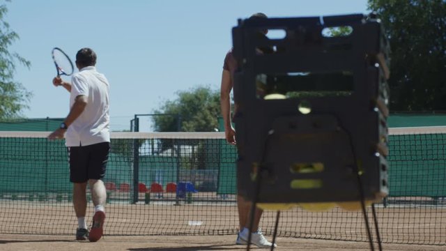 Side view of coach and trainee with tennis rackets standing on court in sunlight and having practice in team