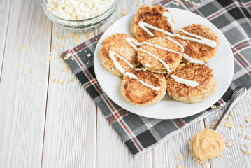 Oat cottage cheese pancakes with sour cream and peanut butter on white wooden background. Healthy breakfast, snack or diner.