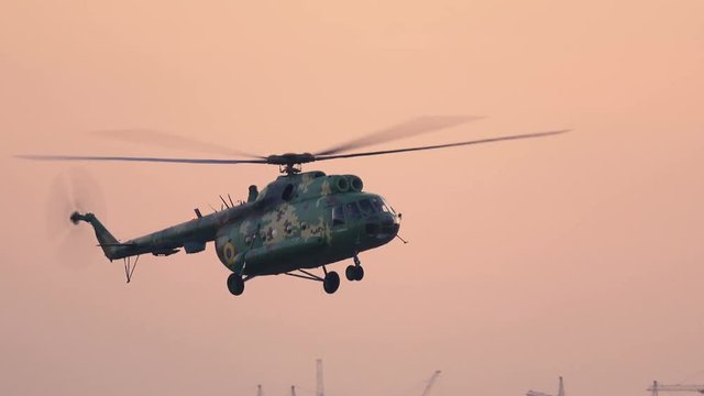 Military helicopter is landing on the take-off field at sunset