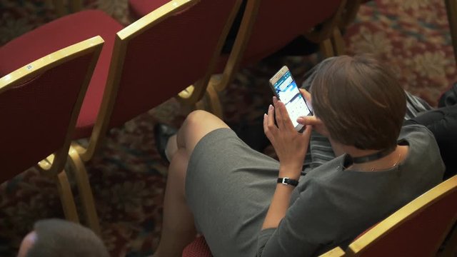 Top view of young woman chatting on smartphone at business conference