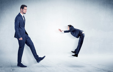 Big businessman kicking small businessman who is flying away with his briefcase on his hand
