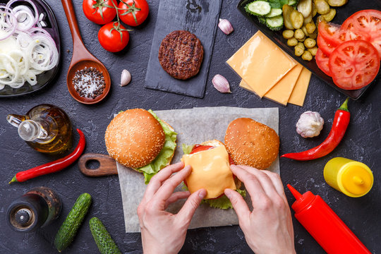 Image on top of two hamburgers, human hands and ingredients