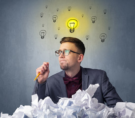 Young businessman sitting behind crumpled paper with lightbulbs above his head