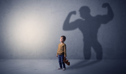 Little waggish boy in an empty room with musclemen shadow behind
