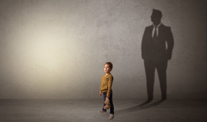 Obraz premium Little boy imagine that he will be businessman and illustrating his future in a big shadow 