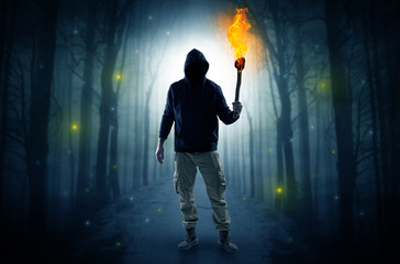Mysterious man coming from a path in the forest with burning flambeau concept
