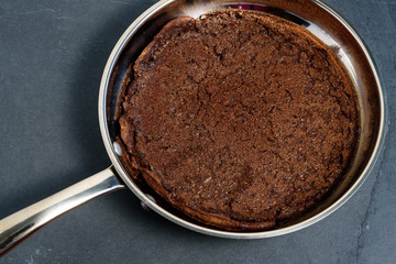 Close up of a Chocolate Dutch Baby pancake fresh out of the oven in a stainless steel frying pan sitting on a slate hot pad
