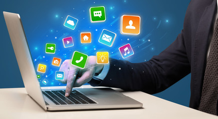 Businessman hand typing on laptop with flying application icons around
