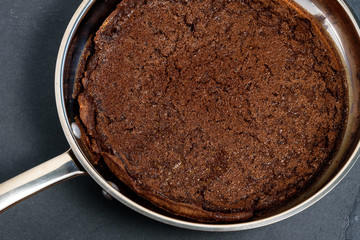 Close up of a Chocolate Dutch Baby pancake fresh out of the oven in a stainless steel frying pan sitting on a slate hot pad
