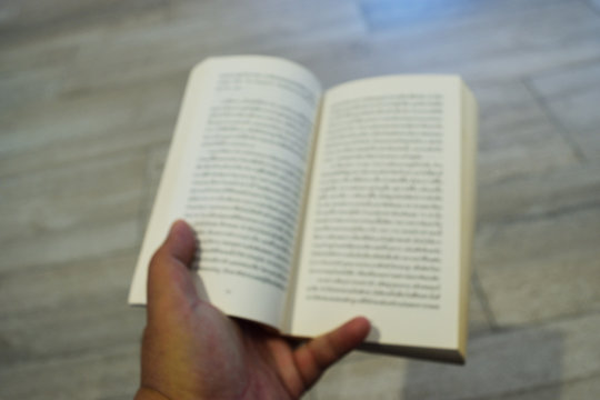 Blur picture of the book unfolded in human hand , Reading activity is being neglected and forgotten , The sight of people with degenerative eye health
