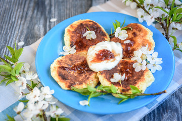 Homemade cottage cheese pancakes on blue plate with spring cherry plum branches on wooden background. Healthy breakfast or snack.
