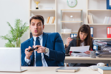 Man playing games in office while colleague is busy