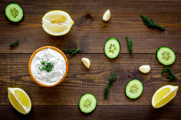 Fototapeta na wymiar Greek yogurt dip with greenery, cucumber, oranges, garlic on dark wooden background top view pattern