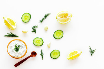 Greek yogurt dip with greenery, cucumber, oranges, garlic on white background top view copy space pattern