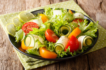 Summer diet food: salad of zucchini, tomatoes, lettuce with lime and spices close-up on a plate on a table. horizontal