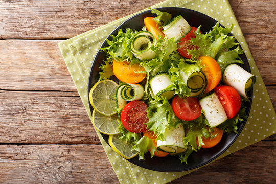 Organic salad of zucchini, tomatoes, lettuce and lime dressed with olive oil close-up on a plate. Horizontal top view