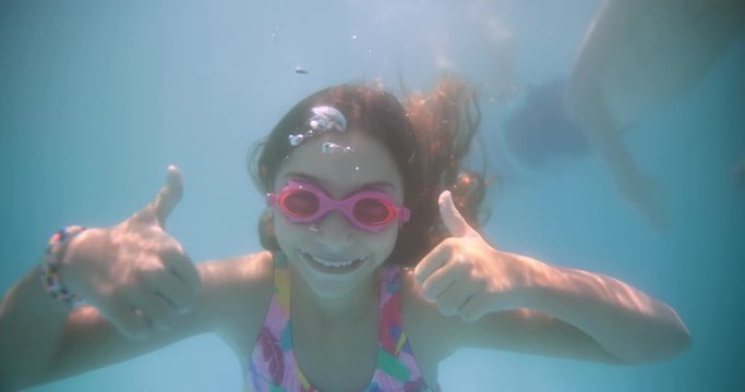 Young girl diving underwater and doing thumbs up sign