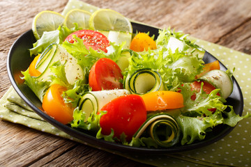 Salad from zucchini, tomatoes, lettuce with lime and spices dressed with olive oil close-up on a plate. horizontal