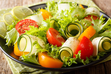 Organic salad of zucchini, tomatoes, lettuce and lime dressed with olive oil close-up on a plate. horizontal