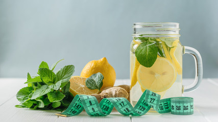 Measuring tape with a mug with a drink of lemon, mint and ginger on a white wooden table.