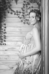 A pregnant woman in a bright sundress in wooden interiors.
