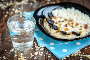 Healthy breakfast: oatmeal with dried fruits and cottage cheese in black plate on dark wooden table.