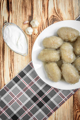 Potato dumplings with stuffed minced meat on a white plate and gravy boat with sour cream on wooden background.
