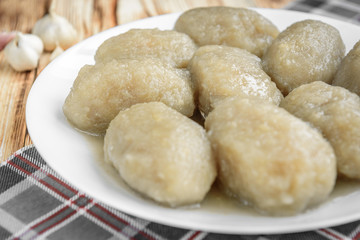 Potato dumplings with stuffed minced meat on a white plate and gravy boat with sour cream on wooden background.