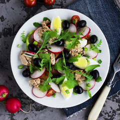 Nicoise salad with tuna, egg, cherry tomatoes and black olives on grey dark background. French cuisine. Top view