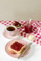 Breakfast of bread toasts with butter and strawberry-rhubarb jam, served with tea. Rustic style.