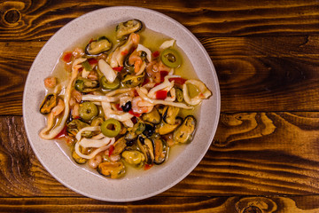 Ceramic plate with different sea food and olives on wooden table. Top view