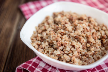 Boiled buckwheat in white bowl on dark wooden table.