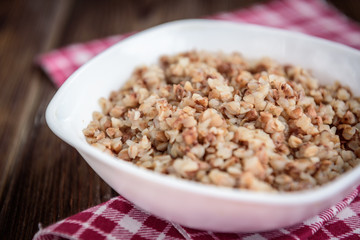Boiled buckwheat in white bowl on dark wooden table.