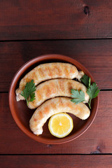Sausages with a grill on a dark wooden background, chicken sausages on a clay bowl, meat dish with lemon, copy space, delicious fast food, american kitchen