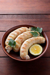 Sausages with a grill on a dark wooden background, chicken sausages on a clay bowl, meat dish with lemon, copy space, delicious fast food, american kitchen