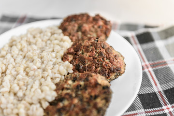 Chicken mushroom cutlets and pearl porridge on white plate on light background. Healthy dinner.