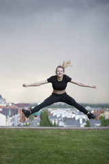 Fototapeta na wymiar Young caucasian girl performs twine jumping over background cityscape