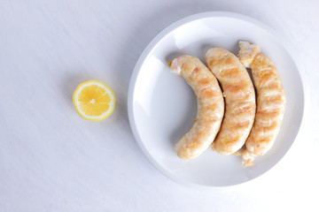 Grilled sausages on white background, chicken sausages on a white plate, meat dish with lemon, copy space, delicious fast food, American cuisine