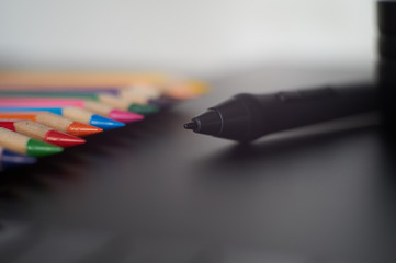 Digital stylus pen on graphic tablet with coloured pencils in ba