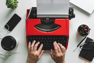 Top view of woman hand working with bright red vintage typewriter