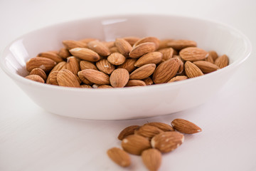 heap of almonds in white dish on white background 