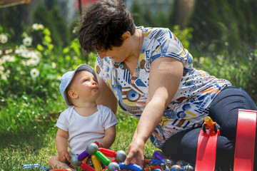 Little baby boy, playing with his grandmother with big construction blocks in garden building shapes