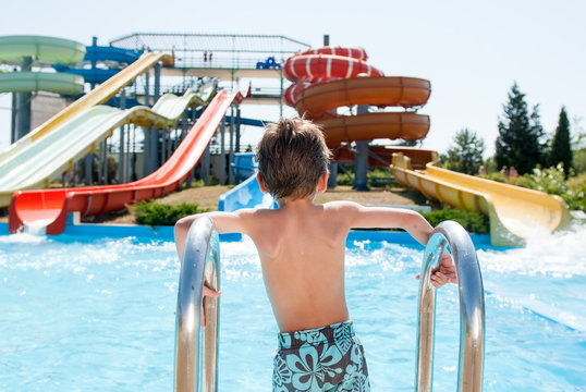 healthy little caucasian boy near blue pool in summer water park outdoors