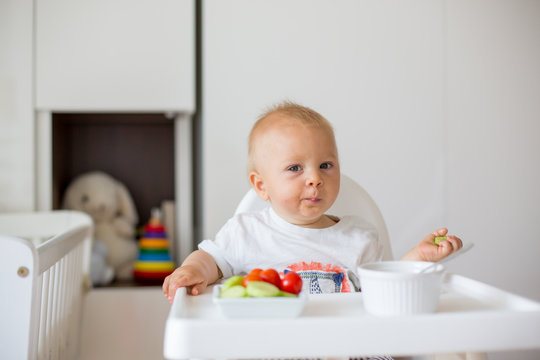 Sweet baby child, boy, eating mashed food and fresh vegetables, sitting in high baby chair