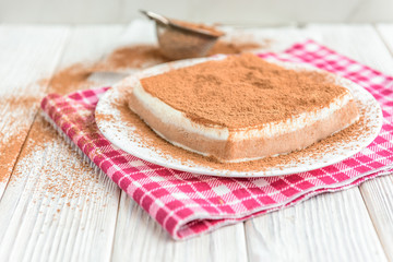 Homemade layered cottage cheese souffle dessert with cocoa on white wooden table